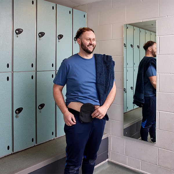 The image shows a man stood in a locker room wearing a SenSura Mio Black bag