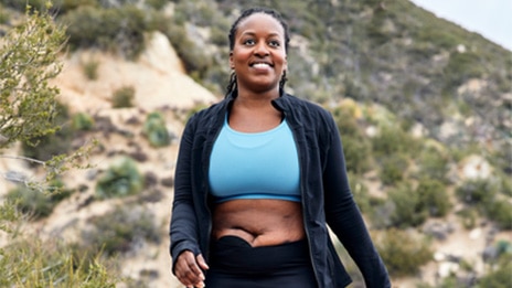 The image shows a woman walking and wearing a SenSura Mio black ostomy bag.