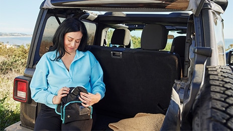 image shows woman sat on the edge of the car, taking her SenSura Mio Black ostomy bags out from her travel bag.